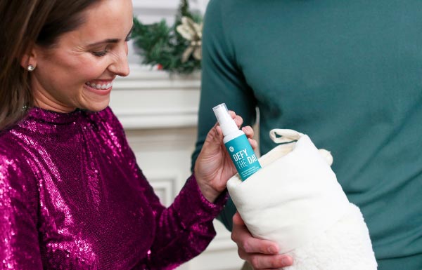 A woman placing a Defy the Day Leave-in Conditioner Spray bottle in a bag for male friend.